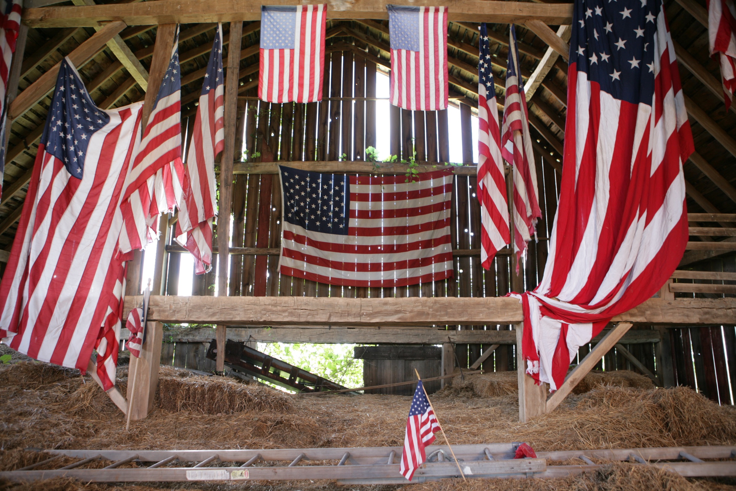 Historic American flags arranged throughout an old wooden barn for the opening of Pershing’s Last Patriot
